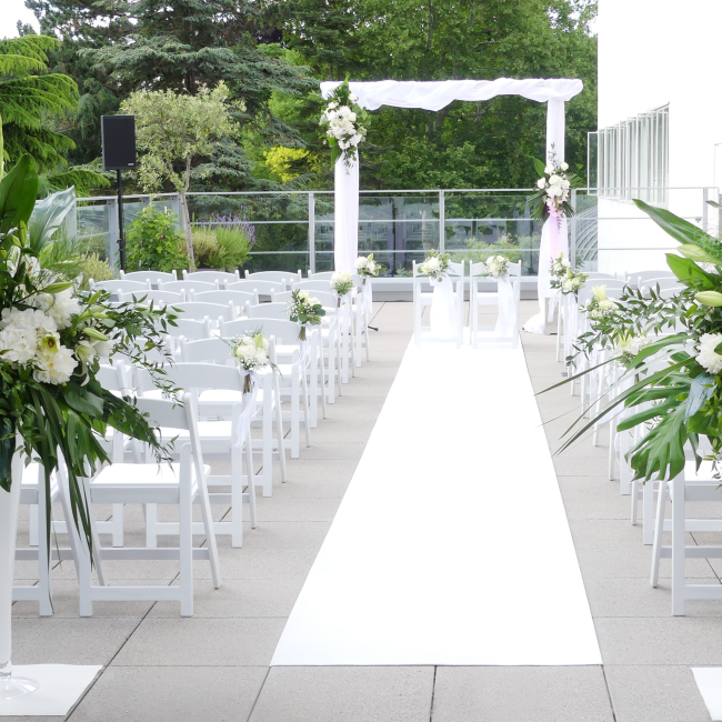 Festlich geschmückte Terrasse für eine Trauung. Die Terrasse ist elegant dekoriert, mit Blumenarrangements, dekorativen Elementen und vielleicht einem weißen Teppich sowie mehreren Stuhlreihen, die den perfekten Rahmen für eine Zeremonie bieten.